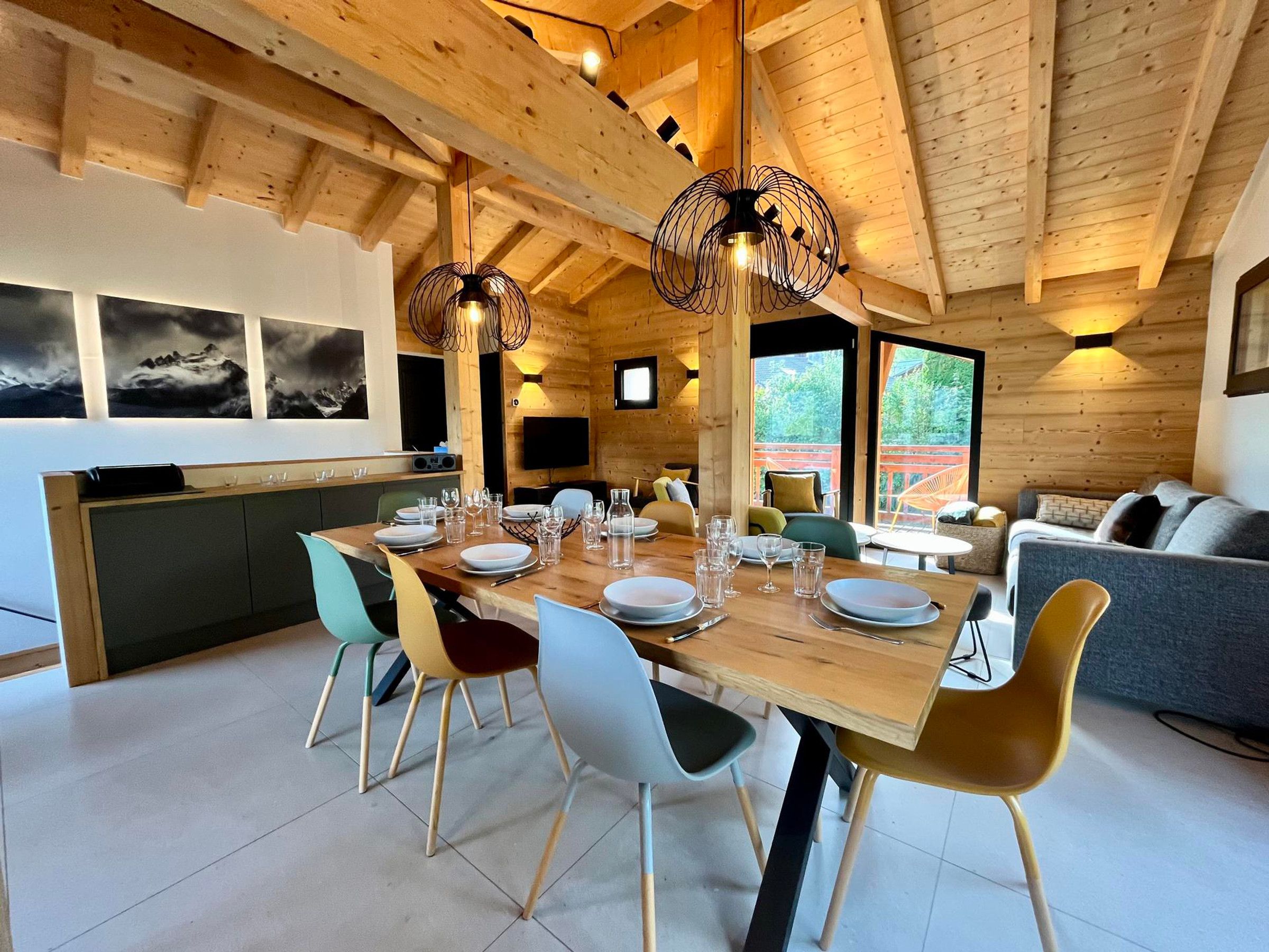 Un interior moderno con techo de madera, una zona de comedor con sillas y mesa puesta, un sofá y un televisor montado en la pared.
