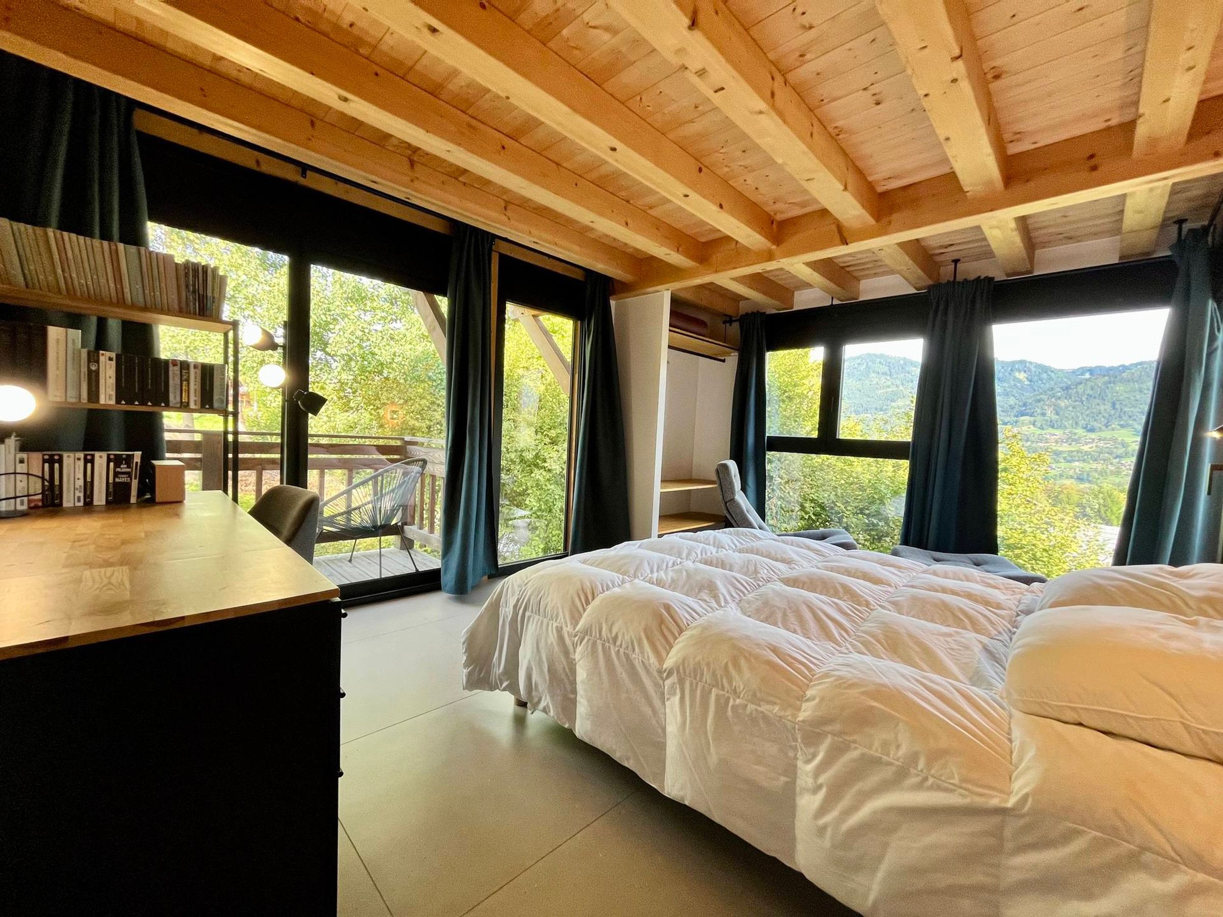 Un dormitorio con una cama grande, un escritorio con libros y vistas al exterior.