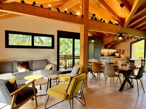 A modern interior with a wooden ceiling, a sofa, yellow chairs, a dining table set, and large windows.