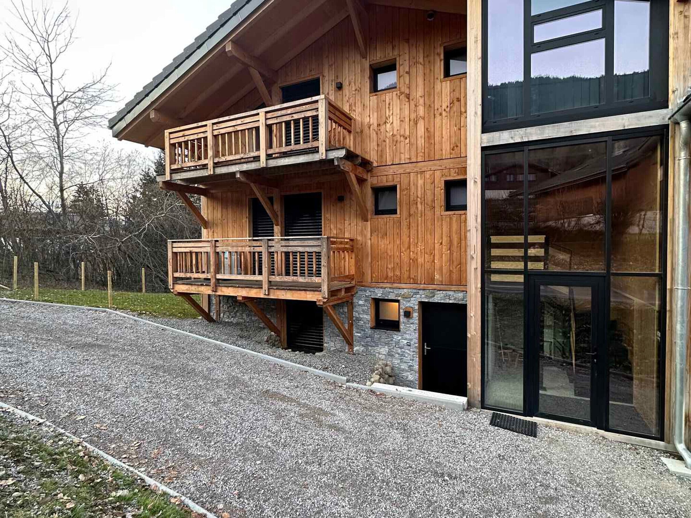 Een houten vakantiehuis met een balkon, stenen fundering en grote ramen.