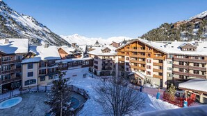 Un resort cubierto de nieve con edificios de varios pisos, una zona de piscina y montañas al fondo.