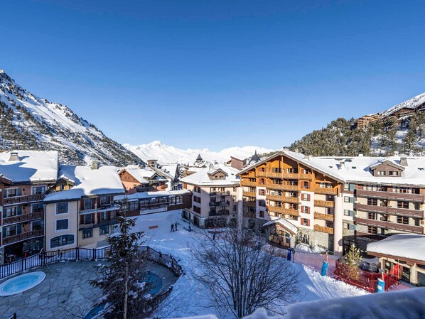 Une station de ski enneigée, avec des bâtiments à plusieurs étages, un espace piscine et des montagnes en arrière-plan.