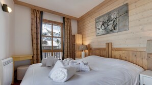 Un dormitorio con una cama grande, paredes de madera, un ventanal con vistas a montañas nevadas y un cuadro en la pared.