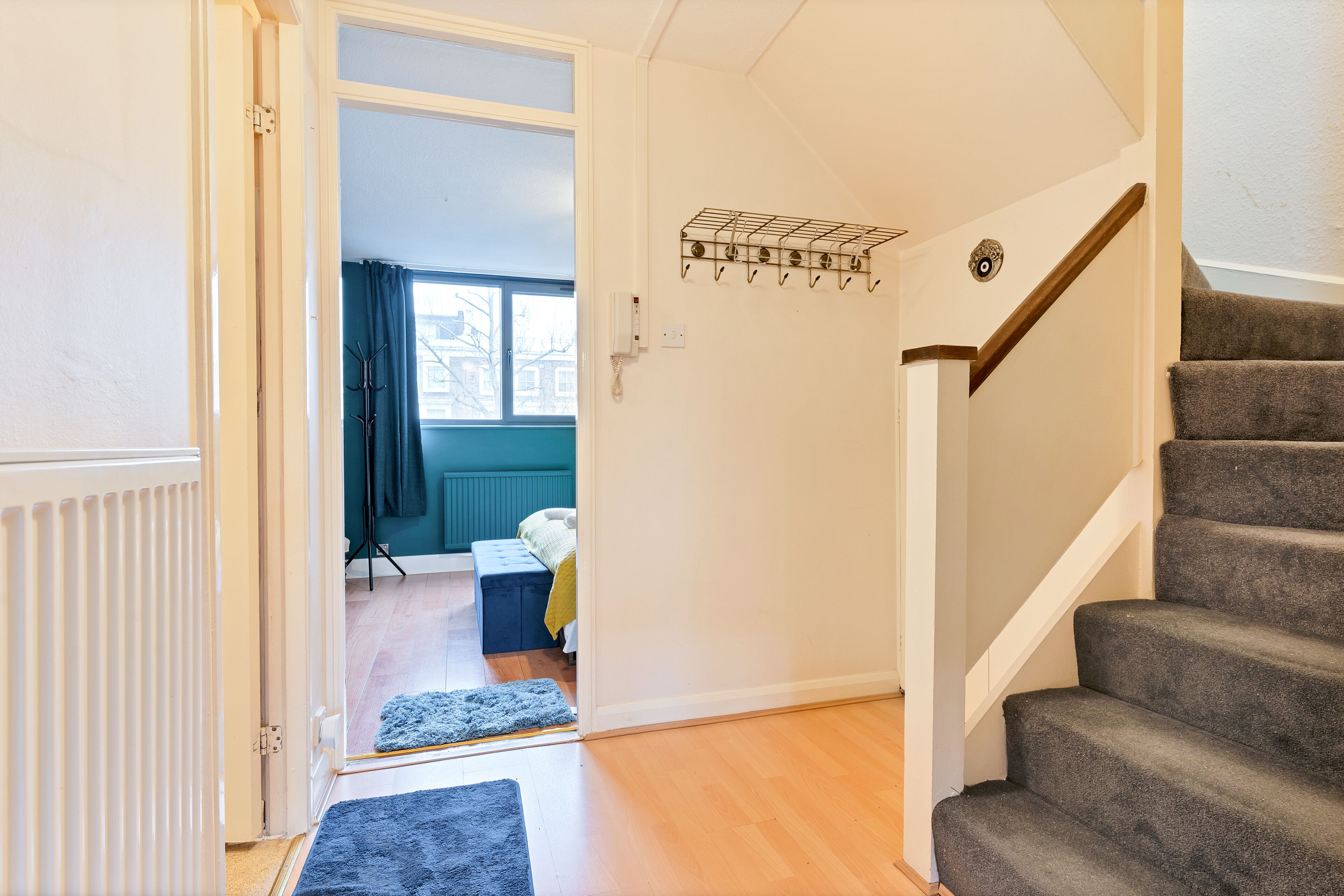 A staircase leading to a bedroom with a bed, a blue rug, and a coat rack.