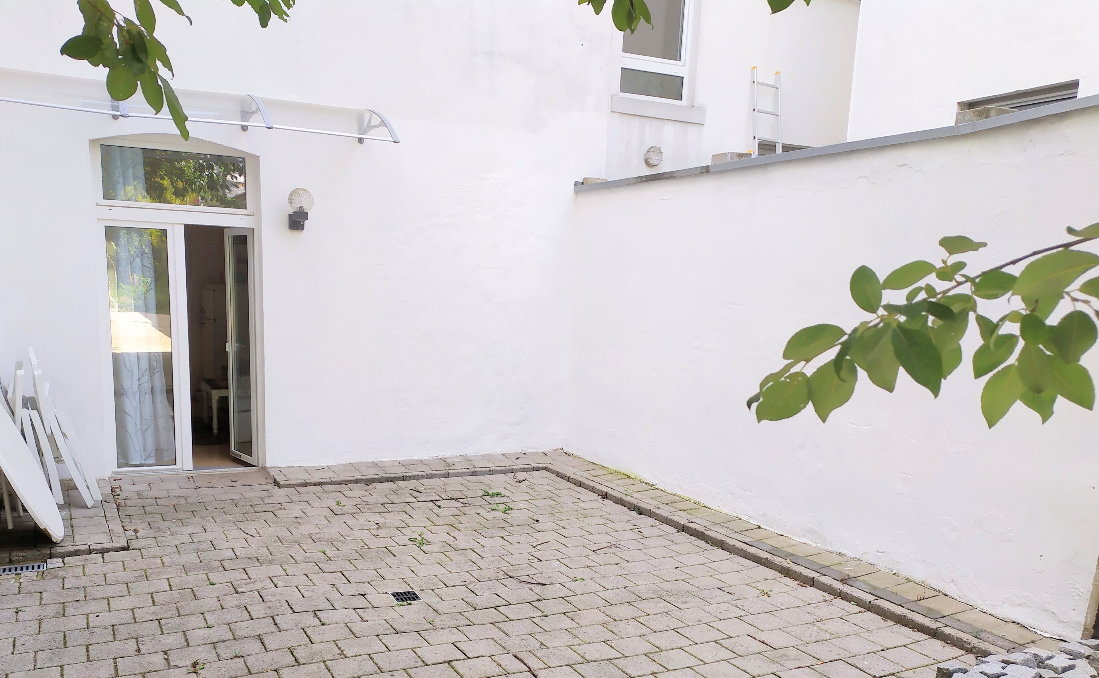 A courtyard with a paved floor, a white wall, and a door leading to a room.