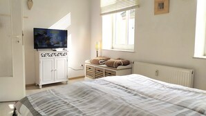 Ein Schlafzimmer mit einem Bett, einem Fernseher auf einem Schrank, einem Fenster mit Jalousien und einer Heizung.