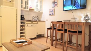 Eine kompakte Küche mit weißen Schränken, einer Kaffeemaschine und einem an der Wand befestigten Fernseher.
