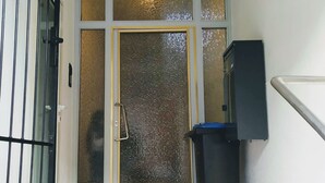 Un pasillo con una puerta de cristal, un bote de basura y una barandilla de metal.