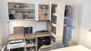 Una cocina compacta con electrodomésticos integrados, repisas abiertas con vajilla y una pequeña zona de encimera.
