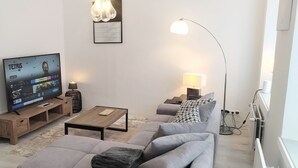 Una sala de estar moderna con un sofá gris, una mesa de centro, un televisor sobre un mueble de madera, una lámpara de pie y un accesorio de iluminación fijado a la pared.