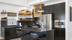 A modern kitchen with dark cabinetry, stainless steel appliances, and a central island with bar stools. - Pet Friendly Home with Hot Tub Near Thunder Ridge & Table Rock Lake (Hollister)