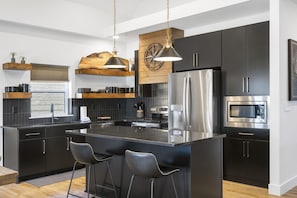 A modern kitchen with dark cabinetry, stainless steel appliances, and a central island with bar stools. - Pet Friendly Home with Hot Tub Near Thunder Ridge & Table Rock Lake (Hollister)
