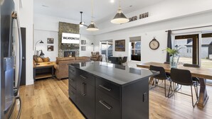 A modern kitchen with a large island, wooden flooring, and a dining area with a table and chairs. - Pet Friendly Home with Hot Tub Near Thunder Ridge & Table Rock Lake (Hollister)