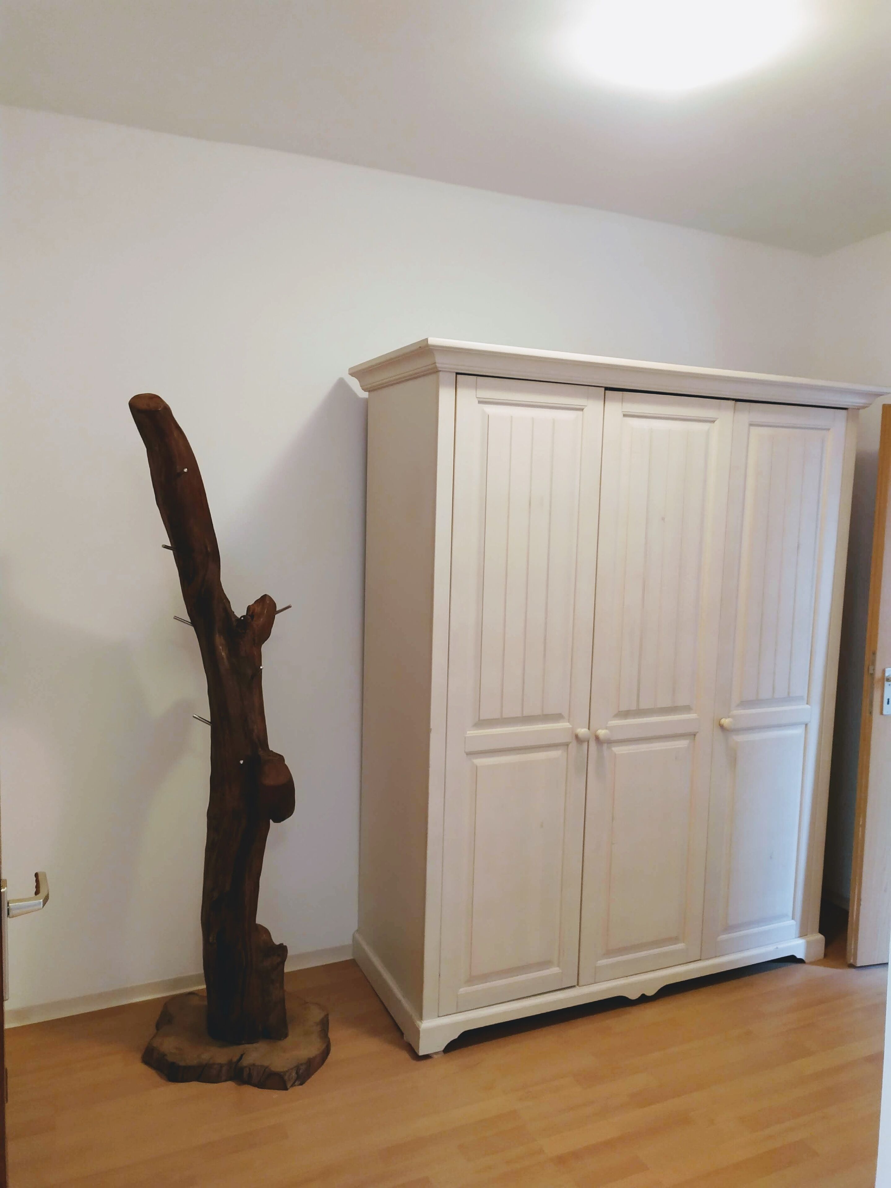 Une pièce avec une armoire blanche, une sculpture en bois et un plancher en bois.