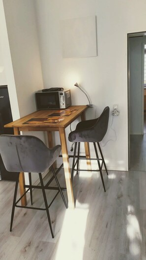 Un coin repas avec une table en bois, deux chaises grises, un four à micro-ondes et une lampe.