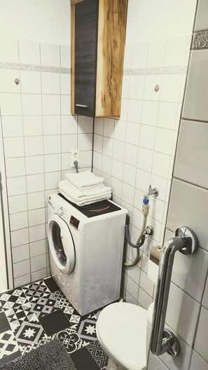 Une petite salle de bain équipée d’un lave-linge, de toilettes et d’un lavabo.