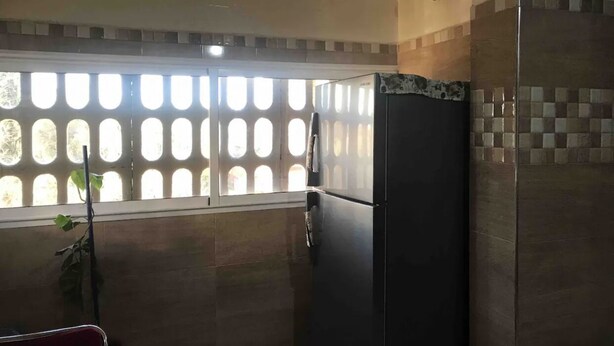 Una cocina con refrigerador, ventana con persiana estampada y salpicadero de azulejos.
