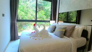 Un lit recouvert d’une courtepointe blanche et orné de deux coussins en forme de cygne, une fenêtre avec des rideaux et une vue sur la verdure à l’extérieur.