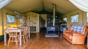 Een rustiek houten interieur met een eettafel, stoelen, een leren bank en een keukenhoek met planken en een fornuis.