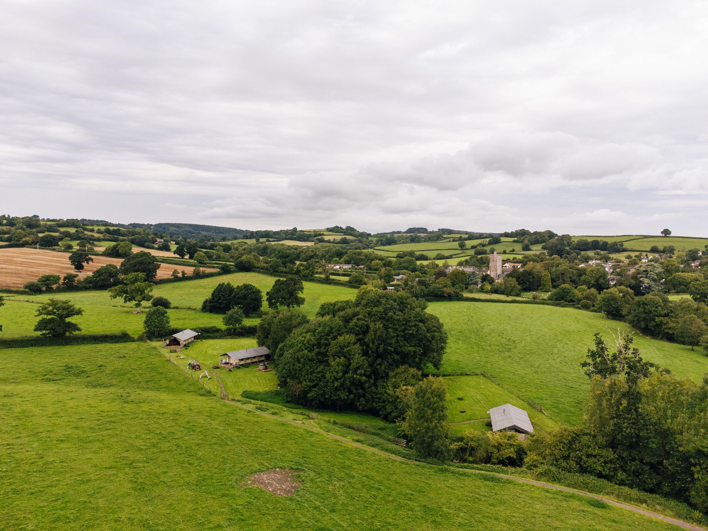 A rural landscape with rolling hills, green fields, and scattered buildings.