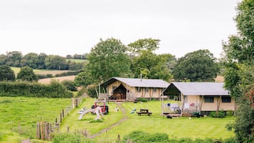 A rustic cabin with a porch, surrounded by a grassy field and trees.