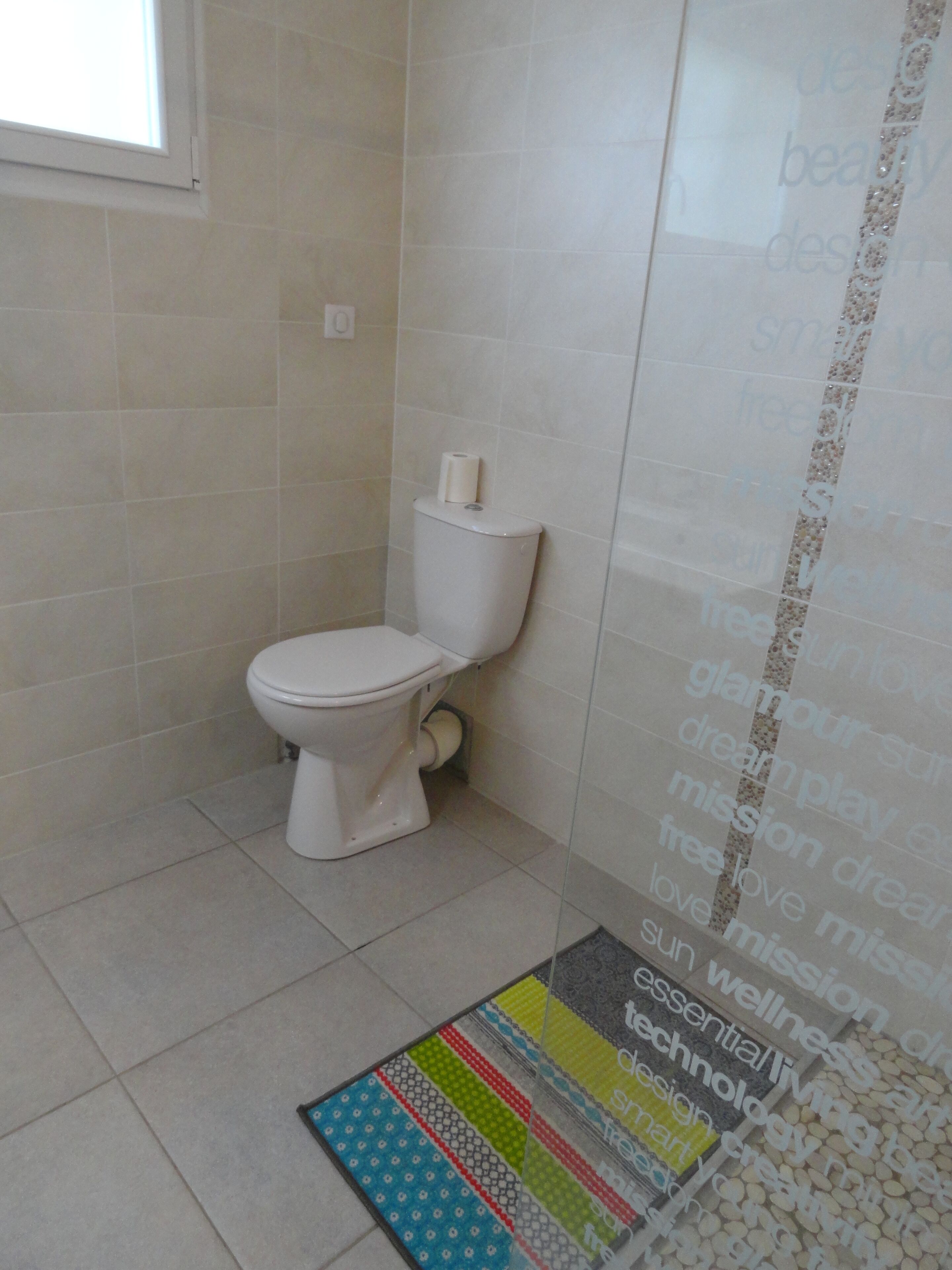 A bathroom with a toilet, a roll of toilet paper on the tank, and a colorful striped rug on the floor.