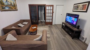 Een woonkamer met een bruine zithoek, een houten salontafel, een flatscreen televisie op een standaard en een deur naar een andere kamer.