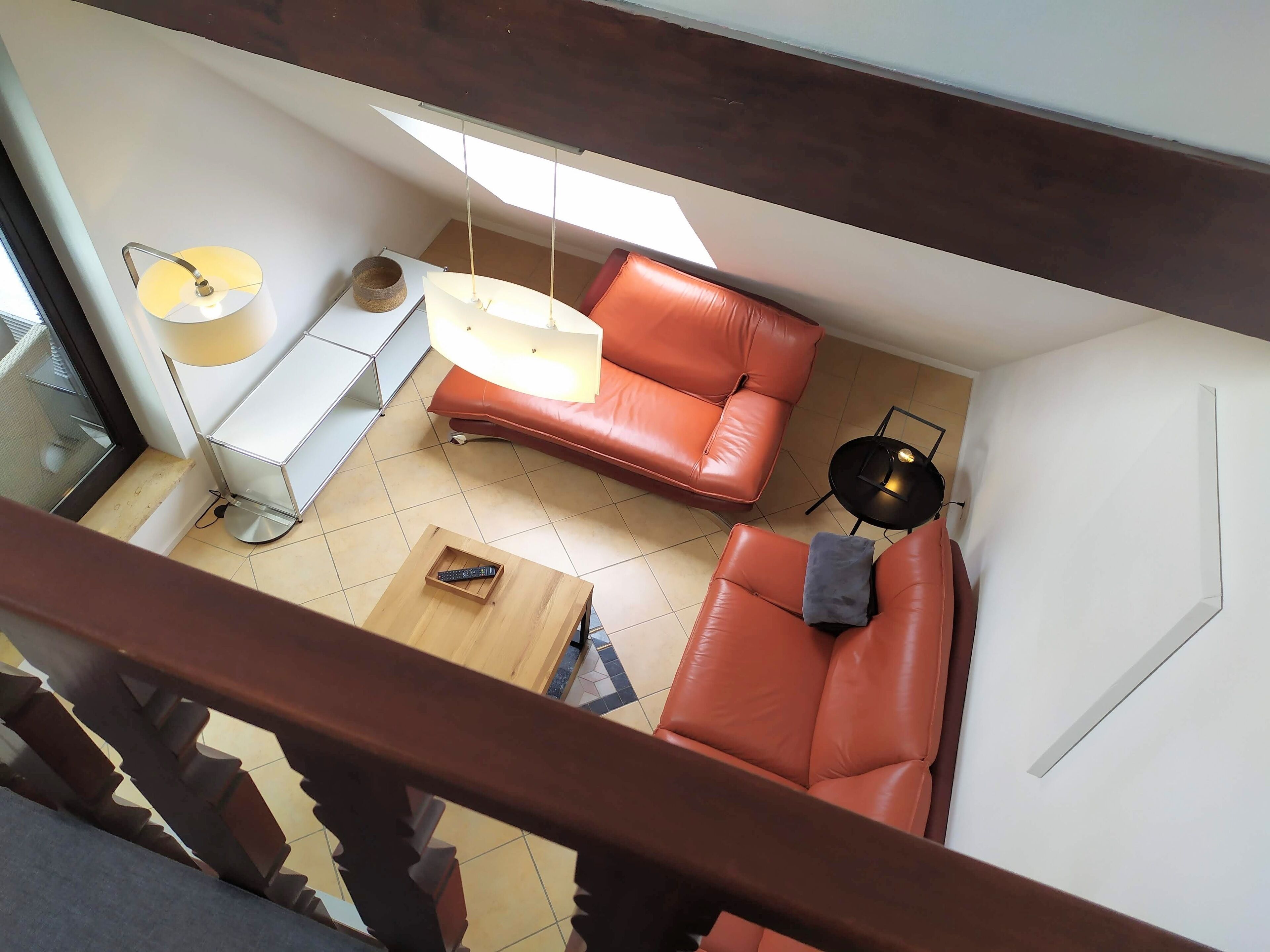 Een moderne woonkamer met een rode leren bank, een houten salontafel en een hanglamp.