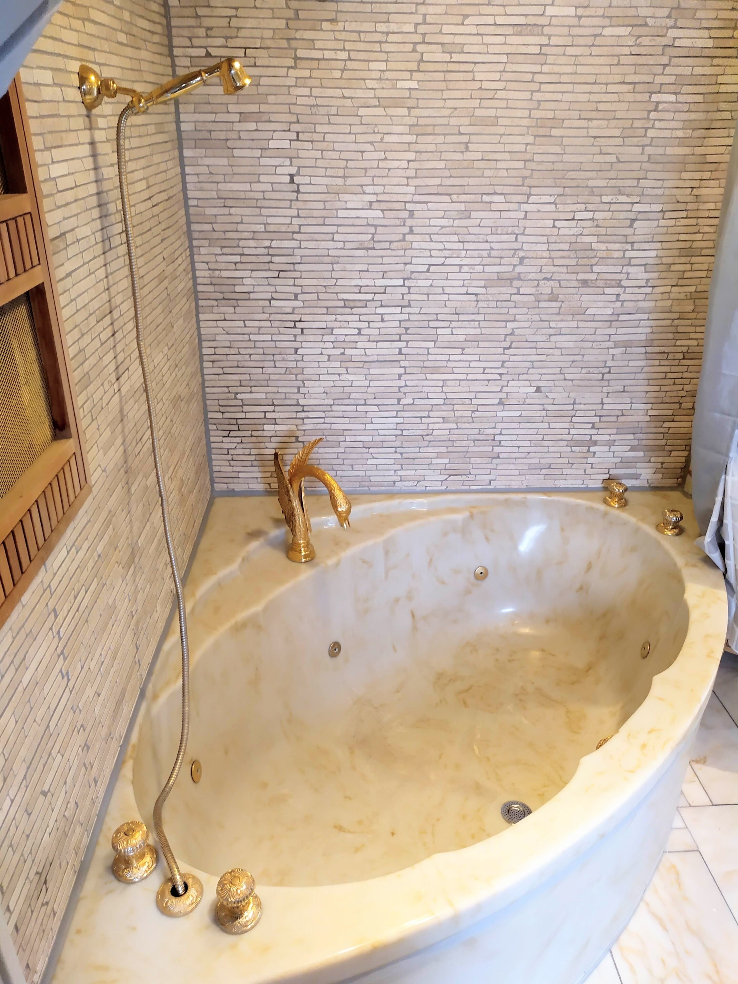 Een groot, ovaal bad met gouden details en douchekop, geplaatst tegen een bakstenen muur.