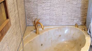 Een groot, ovaal bad met gouden details en douchekop, geplaatst tegen een bakstenen muur.