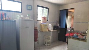 Een compacte keuken met eenvoudige apparaten, een klein krukje en een raam voor natuurlijk licht.