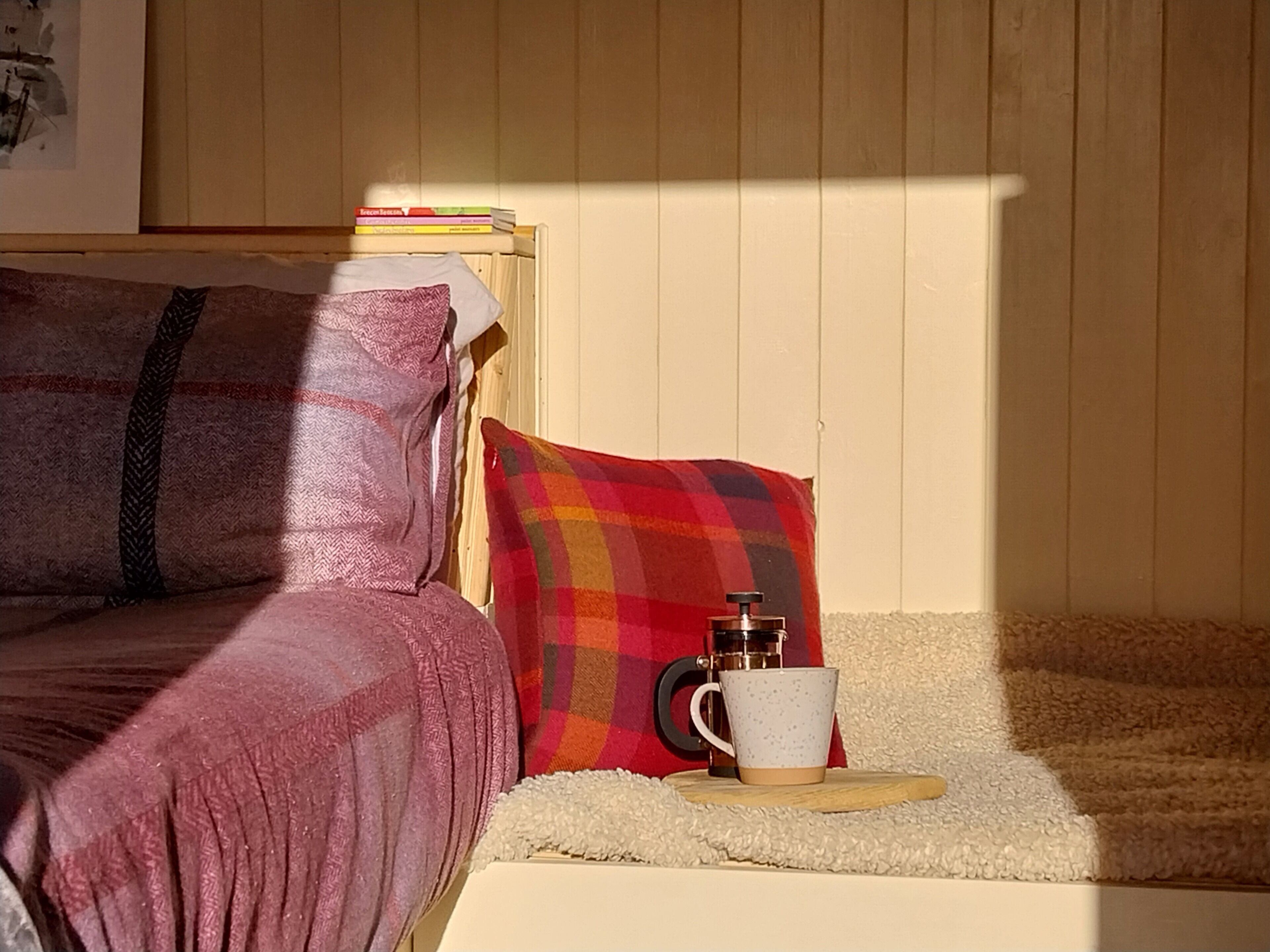 A cozy bedroom with a bed, pillows, a coffee maker, and a cup on a small table.