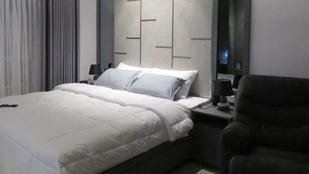 Un dormitorio moderno con una cama grande, mesitas de noche, una silla y un espejo.