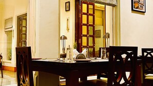 A dining area with a wooden table and chairs, a patterned curtain, and a framed picture on the wall. - The Trishala Vilas Hotel in Ranakpur (Desuri)