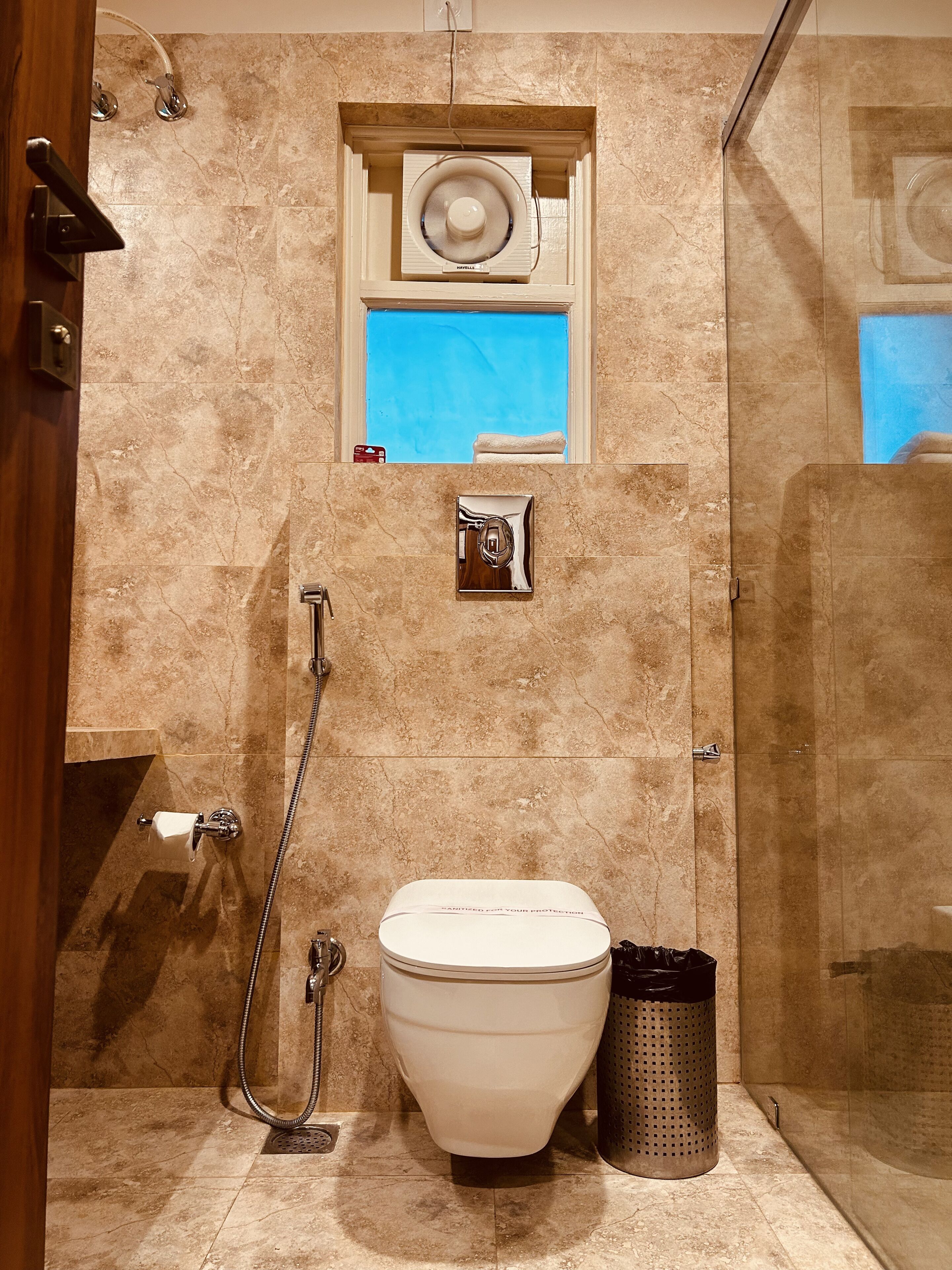 A bathroom with a shower, toilet, and a small window with a towel hanging.