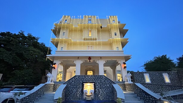 A multi-story building with a traditional architectural style, featuring a central entrance with steps leading up to it, and a decorative fountain at the base. - The Trishala Vilas Hotel in Ranakpur (Desuri)