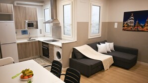 A compact living space with a kitchenette, a dining area with a table and chairs, a sofa, and a washing machine.