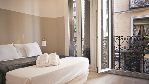 A hotel room with a bed, a lamp, and a view of the outside balcony.