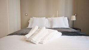 A neatly made bed with white linens and pillows, a gray blanket, and a folded white towel on the bed.