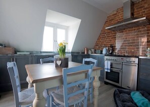 A kitchen with a brick wall, a dining table with chairs, and a stove. - The Loft | Exposed Brick & Fire | Cowdray Views | South Downs | Midhurst High St (Midhurst)