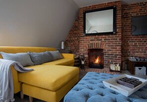 A cozy living room with a yellow sofa, a blue ottoman, and a fireplace. - The Loft | Exposed Brick & Fire | Cowdray Views | South Downs | Midhurst High St (Midhurst)