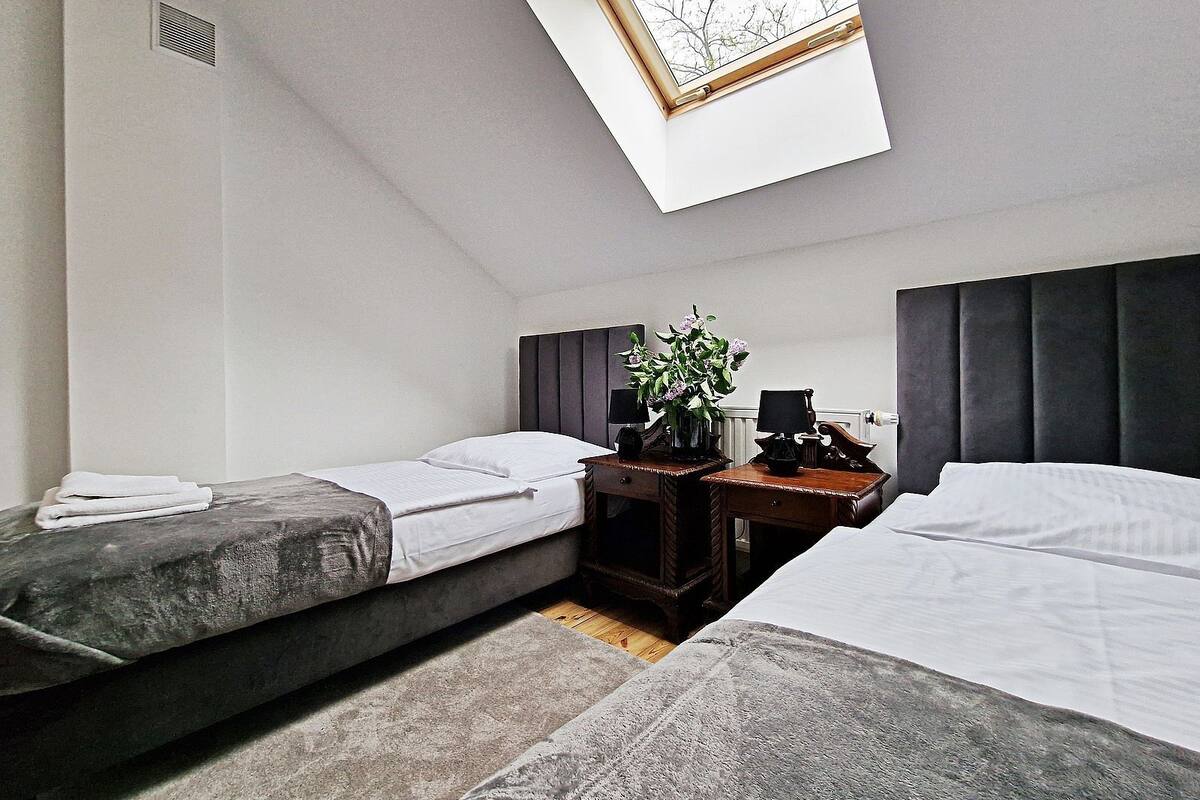A room with two beds, a small table with a vase of flowers, and a skylight above.