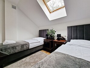 A room with two beds, a small table with a vase of flowers, and a skylight above.
