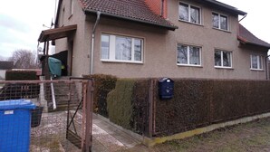 A two-story house with a tiled roof, a fenced yard, and a mailbox. - Ferienwohnung, Besonders für Familien im Oderbruch (Oderaue)