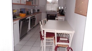 A compact kitchen with white cabinets, a dining table, and chairs. - Ferienwohnung, Besonders für Familien im Oderbruch (Oderaue)