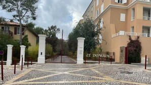 Ein verschlossenes Tor mit einem Kopfsteinpflasterweg, der zu einem Gebäude namens "LE DOMAINT" führt.