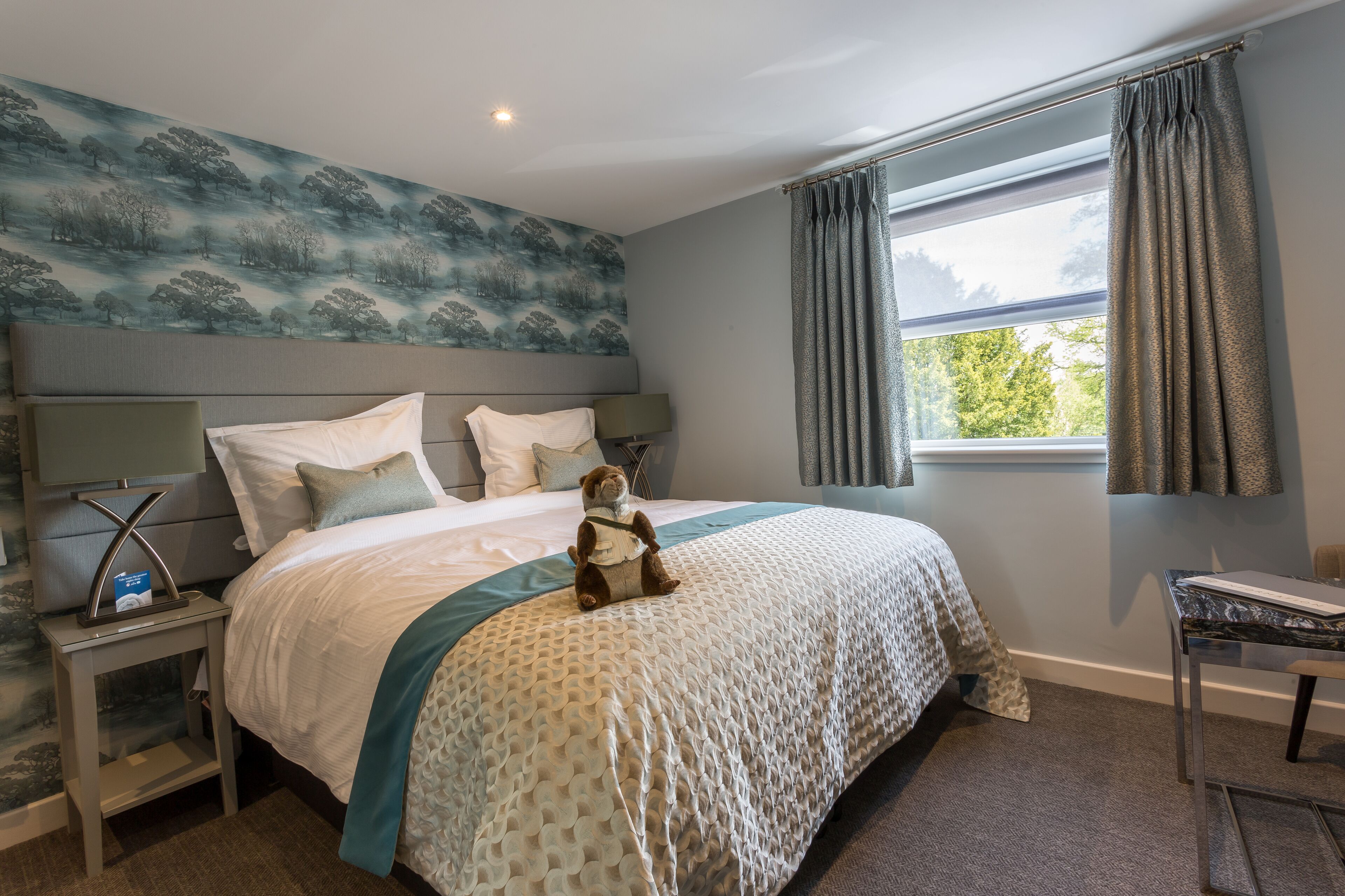 A neatly arranged bedroom with a bed, a nightstand, a desk, and a window with curtains.