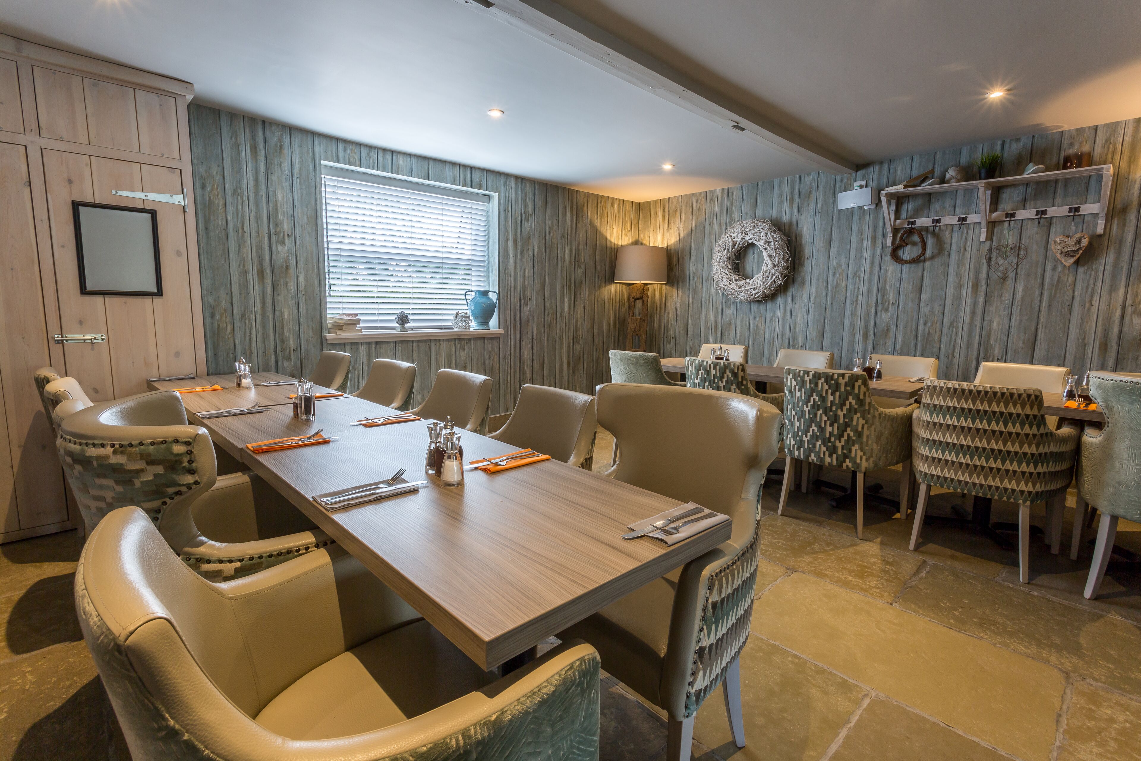 A dining area with a long wooden table, multiple chairs, and a window with blinds.