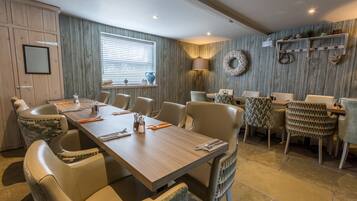 A dining area with a long wooden table, multiple chairs, and a window with blinds.
