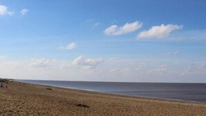 Une vaste plage de sable fin, sous un ciel bleu dégagé et une mer calme.
